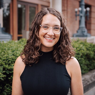 Smiling woman in glasses standing outside building on campus